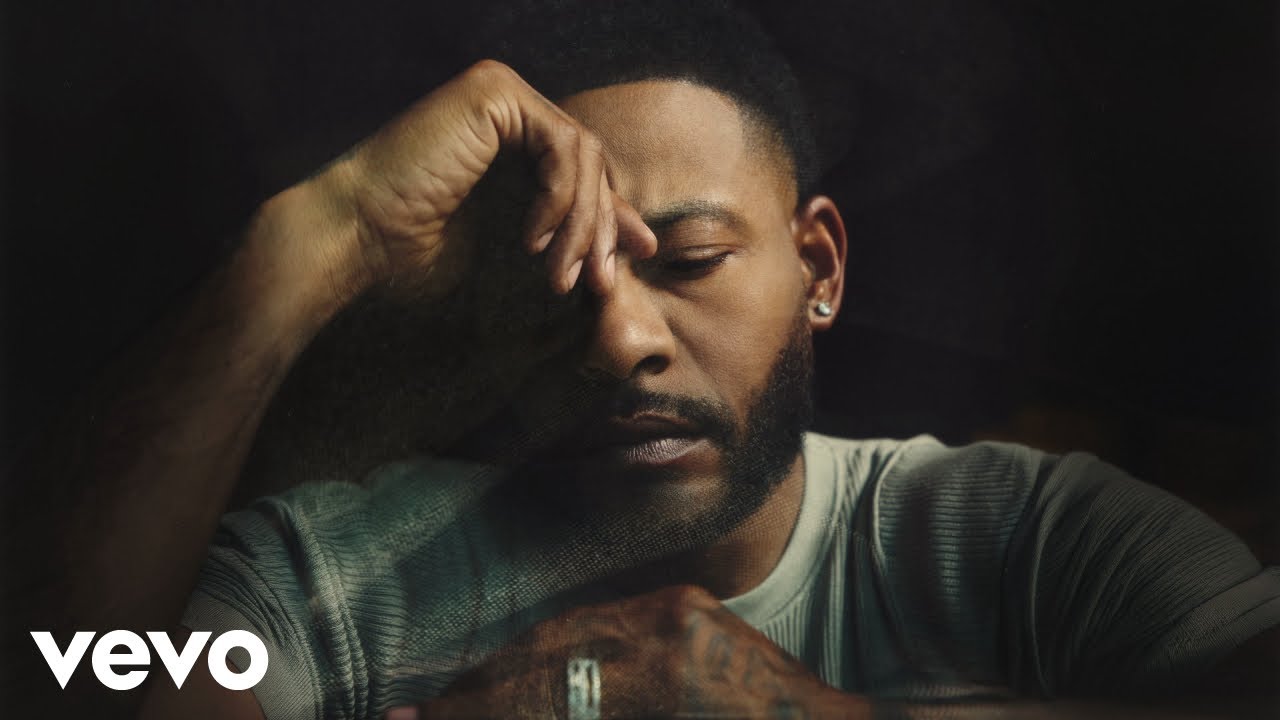 Moody close-up portrait of a man with a beard and short hair, eyes closed, head resting on his hand; Vevo logo appears in the bottom-left corner.