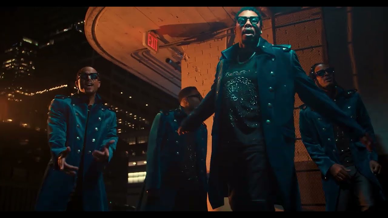 Group of four men in matching blue trench coats and sunglasses pose dramatically at night in a neon-lit urban setting, like a music video scene.