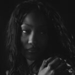 Moody black-and-white portrait of a woman looking to the left, with her hand near her shoulder; Vevo logo in the bottom-left corner.