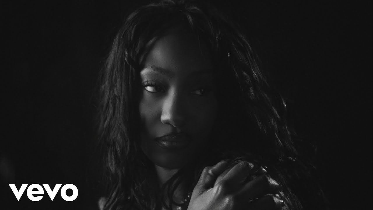 Moody black-and-white portrait of a woman looking to the left, with her hand near her shoulder; Vevo logo in the bottom-left corner.